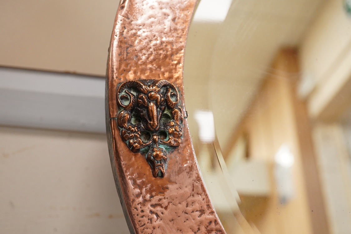 An oval late 19th century hammered copper wall mirror with rams head cartouches, 65cm wide